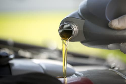 Fresh motor oil being poured into a vehicle engine during an oil change